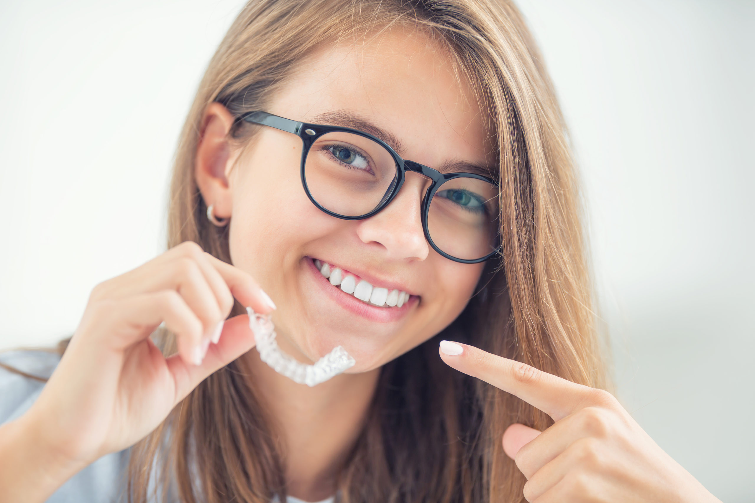 Dental invisible braces or silicone trainer in the hands of a young smiling girl. Orthodontic concept – Invisalign.